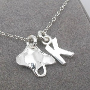 May include: A silver necklace with a manta ray charm and a letter K charm. The necklace is on a gray background.