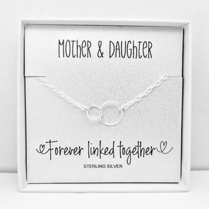 May include: A white box containing a silver necklace. The necklace features two interlocked circles and the inscription "Mother & Daughter Forever linked together" with a heart on each side. The words "Sterling Silver" are printed below the necklace.