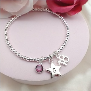 May include: A silver beaded bracelet with a star charm, a crystal charm, and a charm with the number 18. The star charm has the letter S on it.