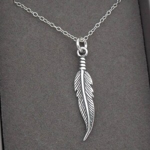 May include: A silver necklace with a feather pendant. The feather is detailed and has a textured surface.