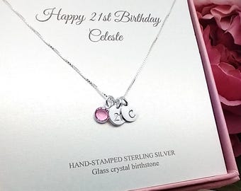 May include: A silver necklace with a pink crystal birthstone and three charms: a '21', a 'C', and another 'C'. The necklace is in a pink gift box with the text 'Happy 21st Birthday Celeste' and 'HAND-STAMPED STERLING SILVER Glass crystal birthstone'.