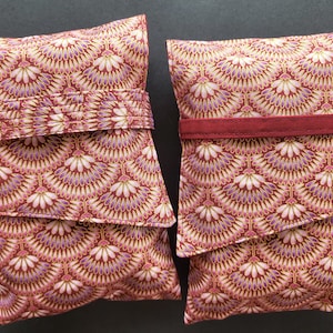 May include: Two rectangular fabric pouches with a repeating fan-like pattern in burgundy, gold, and lavender. One pouch has a burgundy band, the other has a pleated burgundy band. The pouches are likely for storage or organization.