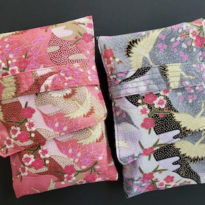 Puede incluir: Dos bolsas de tela con patrones florales y de pájaros. La bolsa de la izquierda es rosa con un patrón floral blanco y dorado. La bolsa de la derecha es gris con un patrón floral blanco, negro y dorado.