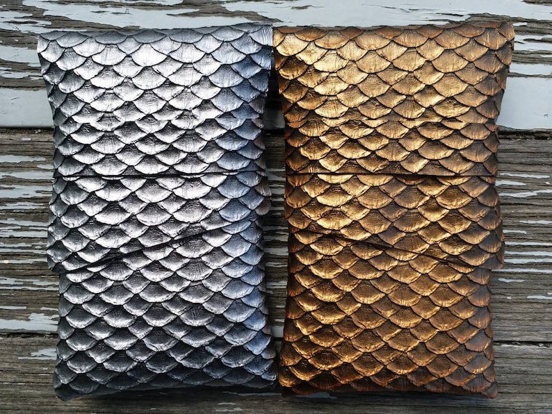 Op de afbeelding: Twee decoratieve zakjes met een schubbenpatroon. Het zakje links is zilver en het zakje rechts is goud.