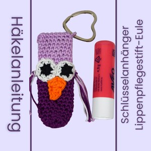 May include: A crocheted owl-shaped keychain holder in light purple and dark purple yarn with white and black eyes and an orange beak. A red lip balm tube labelled 4.8g is placed next to it for scale. The text Häkelanleitung and Schlüsselanhänger Lippenpflegestift-Eule is visible.