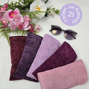 Könnte beinhalten: Fünf Brillenetuis aus Cord in den Farbtönen Burgunder, Lila und Rosa werden gezeigt. Eine Sonnenbrille liegt auf der weißen Oberfläche. Das Bild enthält auch ein Blumenarrangement und eine kreisförmige Grafik mit deutschem Text.