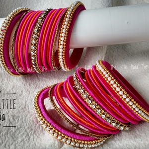 Puede incluir: Un conjunto de brazaletes rosas y naranjas vibrantes, algunos adornados con perlas y pedrería. Los brazaletes están apilados, mostrando su intrincado diseño y variaciones de color. El logotipo de The Little India es visible.