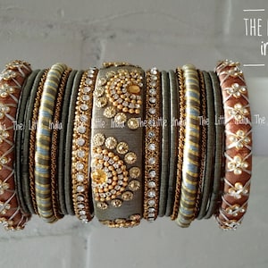 May include: An assortment of decorative bangles in brown, gold, and grey. The bangles feature detailed patterns, rhinestones, and floral motifs. The image includes the text "THE LITTLE india".
