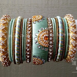May include: A collection of decorative bangles in shades of gold, teal, and silver. The bangles are adorned with intricate embellishments, including rhinestones and floral patterns. The text "The Little India" is visible.