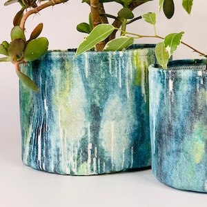 May include: Two fabric plant pots with a blue, green and white abstract pattern. The pots are cylindrical and have a white fabric lining.