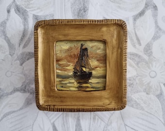 May include: A small, square, framed painting of a sailboat on the water. The painting has a warm color palette of browns, yellows, and oranges, with a textured, gold-colored frame. The artwork depicts a sailboat with its sails up, reflecting in the water.