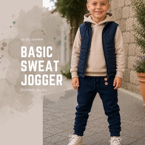 Könnte beinhalten: Eine dunkelblaue Jogginghose mit Kordelzug am Bund und zwei hellen, runden Knöpfen auf der Vorderseite. Die Hose wird mit einem beigen Kapuzenpullover, einer dunkelblauen Steppweste und hellen Stoffschuhen kombiniert.