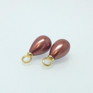 May include: Two brown, teardrop-shaped beads with a metallic finish. Each bead features a gold-coloured ring at the top. These beads are likely intended for jewellery making, possibly for earrings or pendants.