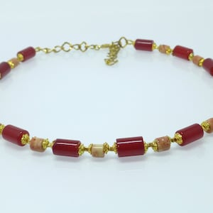 Könnte beinhalten: Eine rote und beige Perlenkette mit einem goldenen Kettenverschluss. Die Perlen sind zylindrisch und haben ein gesprenkeltes Muster.