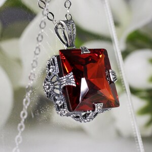 May include: A silver chain necklace with a red gemstone pendant. The pendant is set in a filigree design.