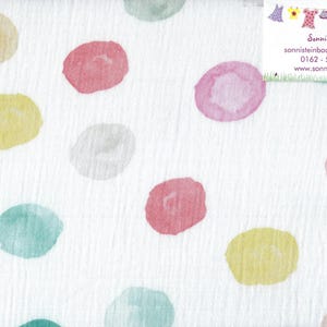 Könnte beinhalten: Weißer Stoff mit einem Muster aus großen Polka-Dots im Aquarellstil in verschiedenen Farben, darunter Gelb, Rosa, Grün und Lila. Der Stoff hat ein strukturiertes Aussehen. Ein Lineal ist am rechten Rand sichtbar.