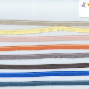 Könnte beinhalten: Eine Sammlung von 10 verschiedenen elastischen Bändern in verschiedenen Farben, jedes etwa 1,2 cm breit. Die Bänder sind in Reihen auf einem weißen Hintergrund angeordnet. Die Farben sind beige, gelb, rosa, orange, grau, braun, blau und türkis.