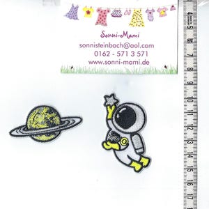 Könnte beinhalten: Zwei gestickte Bügelbilder: ein gelber und schwarzer Planet mit einem Ring und ein weißer Astronaut, der einen Stern hält. Die Patches befinden sich auf einem weißen Hintergrund.