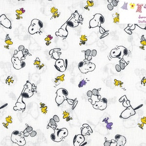 Könnte beinhalten: Weißer Stoff mit einem sich wiederholenden Muster von Snoopy- und Woodstock-Charakteren in Schwarz, Gelb und Lila. Die Cartoon-Figuren sind in verschiedenen Posen, was ein verspieltes Design ergibt. Der Stoff eignet sich für verschiedene Bastelprojekte.