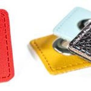 Könnte beinhalten: Rote, gelbe, hellblaue und schwarze quadratische Ösen mit silbernen Metallösen. Die rote Öse wird separat gezeigt, während die anderen gestapelt sind. Die Ösen haben einen genähten Rand.