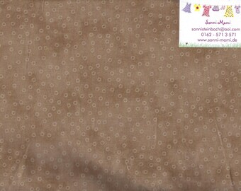 May include: Brown fabric with a repeating pattern of small, light-colored circles. A white card with text and a ruler are visible on the right side. The fabric has a textured appearance.