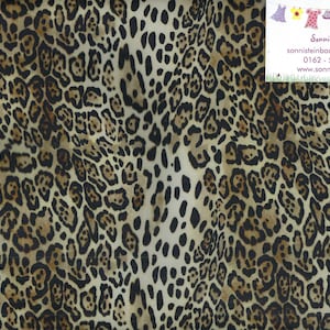 Könnte beinhalten: Stoff mit Leopardenmuster. Der Stoff hat einen beigefarbenen Hintergrund mit dunkelbraunen und schwarzen Flecken. Ein Lineal mit Zentimetermessungen ist am rechten Rand zu sehen. Ein kleines weißes Etikett mit Text befindet sich oben rechts.