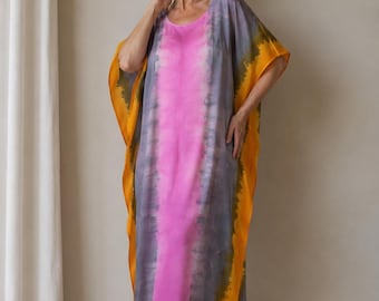Puede incluir: Un vestido caftán largo hasta el suelo con un vibrante patrón tie-dye. El panel central es de color rosa brillante, flanqueado por bandas verticales de gris apagado, y acabado con bordes anchos de color amarillo dorado sólido.