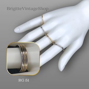 Può includere: Esposizione di anelli in tonalità oro e argento su una mano di manichino bianca. Gli anelli variano nello stile, con fasce sottili e design impilati. L'immagine include il testo "BrigitteVintageShop" e "RG 51".