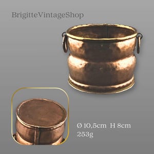 May include: A hammered copper bucket with a brass rim and two side ring handles. The bucket features a rounded body and a flat base. Text on the image includes BrigitteVintageShop, a diameter of 10.5 cm, a height of 8 cm, and a weight of 253 g.