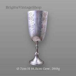 Könnte beinhalten: Ein silberfarbener Kelch mit floralen Gravuren. Der Kelch hat eine breite, abgerundete Schale, einen schlanken Stiel und einen ausgestellten Fuß. Der Text "BrigitteVintageShop" steht oben. Der Kelch hat 7 cm Durchmesser, 18,5 cm Höhe und wiegt 269 g.