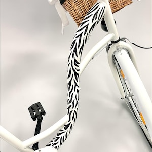 May include: A white bicycle with a wicker basket and black and white zebra print detailing on the frame. The bicycle has black handlebars and pedals. The tyres are white with silver spokes.