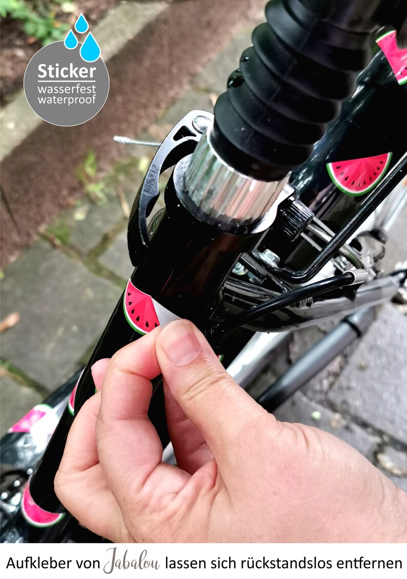 May include: A close-up of a black bicycle handlebar with a watermelon sticker. The sticker is being peeled off to reveal the black handlebar underneath. The sticker is labeled "Sticker wasserfest waterproof". The text "Aufkleber von Jabalou lassen sich r&uuml;ckstandslos entfernen" is visible at the bottom of the image.