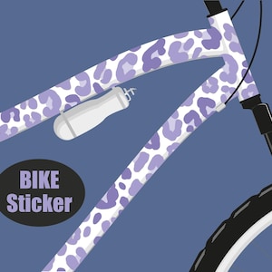 Könnte beinhalten: Fahrradrahmen mit weißem und lila Leopardenmuster. Das Bild zeigt einen Teil des Fahrrads, einschließlich Lenker, Wasserflasche und Reifen. Der Text "BIKE Sticker" befindet sich auf einem schwarzen Oval.