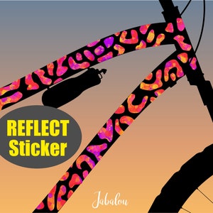 Könnte beinhalten: Ein schwarzer Fahrradrahmen mit einem reflektierenden Aufkleber in Pink, Orange und Gelb. Der Aufkleber trägt den Text "Reflect Sticker". Der Fahrradrahmen ist vor einem Sonnenuntergangs-Hintergrund silhouettiert.