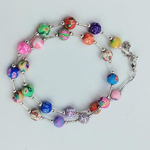 Könnte beinhalten: Eine mehrfarbige Perlenkette mit einer silbernen Kette und einem Verschluss. Die Perlen sind rund und haben ein Blumenmuster.