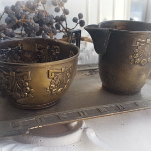 Könnte beinhalten: Ein antikes Set aus Kanne und Zuckerdose aus Messing mit verzierten Blumendesigns. Das Set wird auf einem passenden Tablett aus Messing präsentiert.