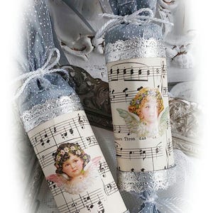 Könnte beinhalten: Zwei blaue und silberne Weihnachtscracker vor weißem Hintergrund. Jeder Cracker ist mit einem Vintage-Notenblatt-Design verziert, das einen Engel mit Flügeln und einer Blumenkrone zeigt. Der Text auf dem Cracker lautet "Himmels Thron das".