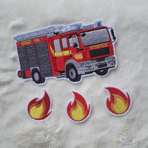 Może przedstawiać: Haftowane naszywki przedstawiające czerwoną straż pożarną z żółtymi akcentami i napisem "Feuerwehr". W zestawie znajdują się również trzy naszywki z płomieniami. Naszywki mają białą obwódkę.