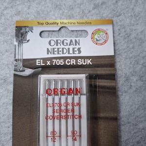 Könnte beinhalten: Eine Packung Organ-Nadeln für Overlock- und Coverstich-Nähmaschinen. Die Packung ist rot, weiß und schwarz und trägt den Text "Organ Needles" und "EL x 705 CR SUK". Die Nadeln befinden sich in einem durchsichtigen Kunststoffgehäuse und sind mit den Größen 80/12 und 90/14 gekennzeichnet.