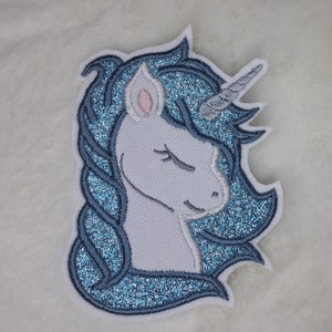 Könnte beinhalten: Ein blauer und weißer Glitzer-Aufbügel-Patch mit einem Einhorn mit geschlossenem Auge und einem Horn.