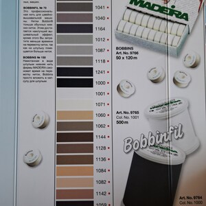 May include: A color chart of Madeira Rayon and Bobbinfil thread spools. The chart shows 15 different colors of thread, ranging from light beige to black. The spools are labeled with the thread number, color number, and length. The chart also includes the text "Rayon" and "Bobbinfil".
