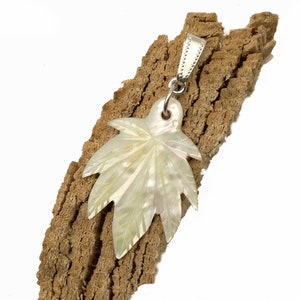 Könnte beinhalten: Ein weißer Perlmutt-Blatt-Anhänger mit einer silbernen Öse. Das Blatt ist mit komplizierten Details geschnitzt und hat einen natürlichen irisierenden Glanz.