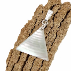 Pode incluir: Um pingente triangular feito de madrepérola branca iridescente com uma superfície lisa e polida. O pingente apresenta um passador de metal prateado preso ao canto superior, permitindo que seja suspenso por uma corrente ou cordão.