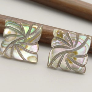 May include: A pair of iridescent abalone shell earrings with a carved floral design. The earrings are square shaped and have a light green, blue, and gold colour.
