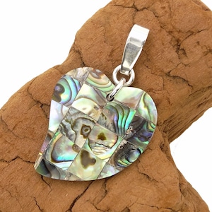 Könnte beinhalten: Herzförmiger Anhänger mit einem Mosaikdesign aus schillernden Abalone-Muschelteilen. Der Anhänger hat eine silberne Öse zum Anbringen an einer Kette. Die Muschelteile zeigen eine Reihe von Farben, darunter Grün, Blau und Gold.