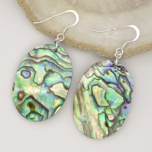 May include: A pair of silver dangle earrings with oval-shaped abalone shell pendants. The shells have a green, blue, and iridescent color pattern.