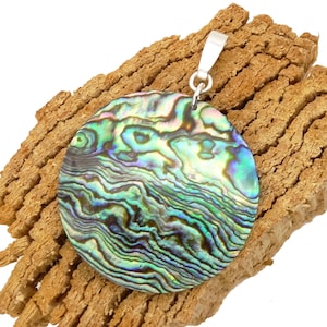 Könnte beinhalten: Runder, schillernder Abalone-Muschel-Anhänger mit silberner Öse. Der Anhänger zeigt wirbelnde Muster in Grün, Blau und Lila. Er liegt auf einer strukturierten, braunen, rindenartigen Oberfläche.