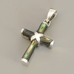 Pode incluir: Um pingente de cruz de prata com incrustações de madrepérola preta e verde.