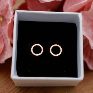 Könnte beinhalten: Ein Paar Ohrstecker aus Roségold in Form von Kreisen in einer weißen Schachtel mit schwarzem Innenraum.