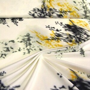 Könnte beinhalten: Ein Stück cremeweißer Stoff mit einem Druckmuster aus dunkelgrauen, tintenartigen botanischen Silhouetten und leuchtend gelben Aquarell-Spritzern. Das Material ist in der Mitte gerafft, wodurch weiche Falten und tiefe Schatten entstehen.